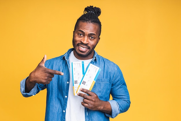 Jeune homme noir afro-américain souriant heureux tenant des billets d'embarquement isolés sur fond jaune.