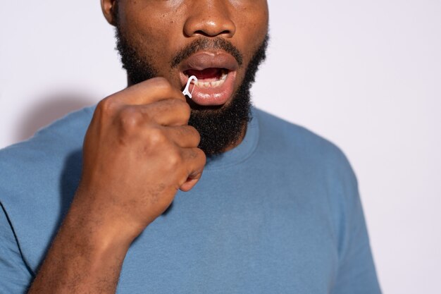 Jeune homme noir à l'aide d'un fil dentaire pour nettoyer ses dents en gros plan