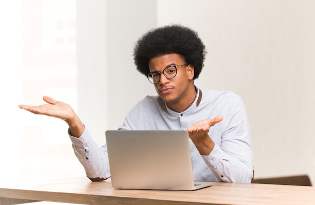 Jeune homme noir à l'aide de son ordinateur portable confus et douteux