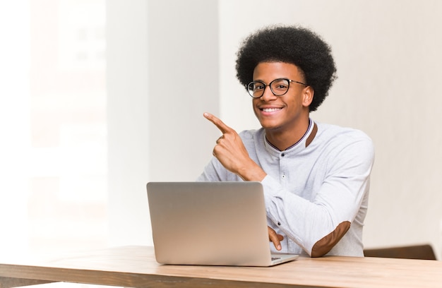 Jeune homme noir à l'aide de son ordinateur portable en souriant et pointant sur le côté