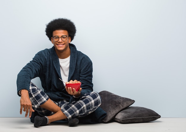 Jeune homme noir assis et prenant un petit déjeuner gai avec un grand sourire