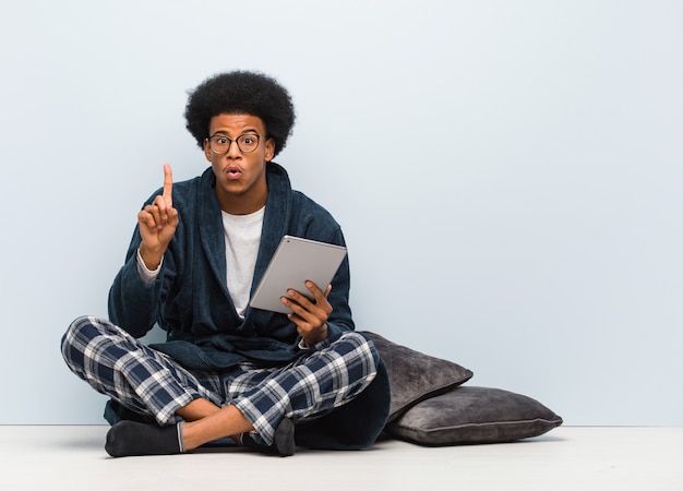 Jeune homme noir assis sur sa maison et tenant sa tablette ayant une excellente idée, concept de créativité