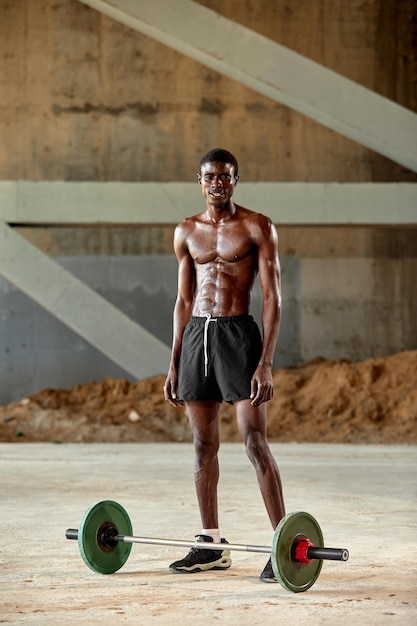 Jeune homme noir athlétique soulevant une barre de poids lourd dans une salle de sport en plein air sous le pont Concept de mode de vie sain