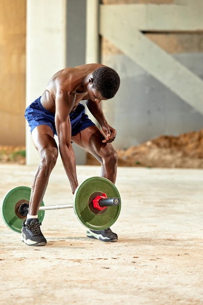 Jeune homme noir athlétique soulevant une barre de poids lourd dans une salle de sport en plein air sous le pont Concept de mode de vie sain