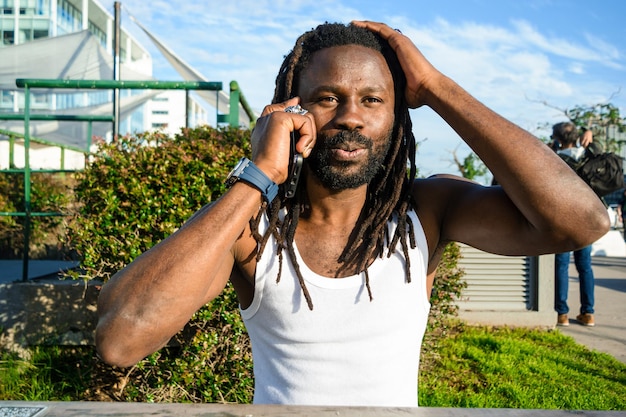 Jeune homme noir avec barbe et dreadlocks choqué de parler au téléphone avec une main sur la tête