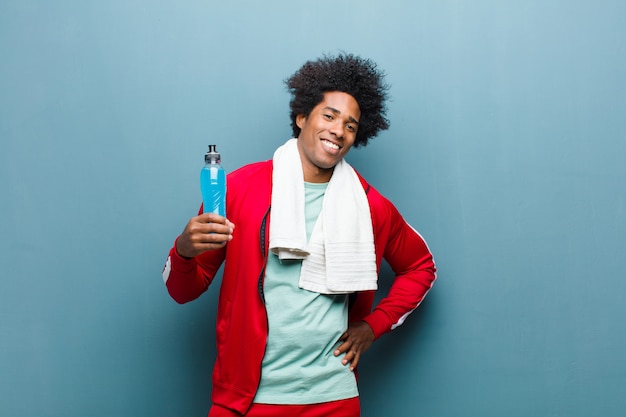 Jeune homme noir avec une boisson sportive contre le mur bleu grunge