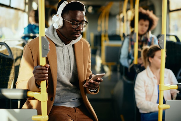 Photo jeune homme noir avec un casque à l'aide d'un téléphone intelligent tout en se déplaçant en bus