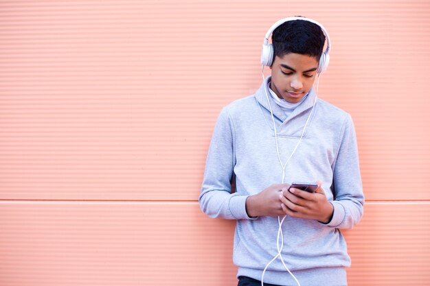 Un jeune homme noir écoute de la musique sur son téléphone portable tout en restant dans la rue. Adolescent afro-américain dans les écouteurs à l&#39;aide d&#39;un smartphone.