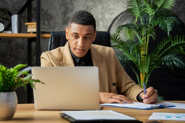 Un jeune homme noir est assis au bureau et regarde attentivement l'écran de l'ordinateur portable homme d'affaires sitti