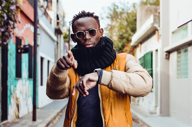 Jeune homme noir à l'extérieur pointant vers la caméra indiquant l'heure de commencer