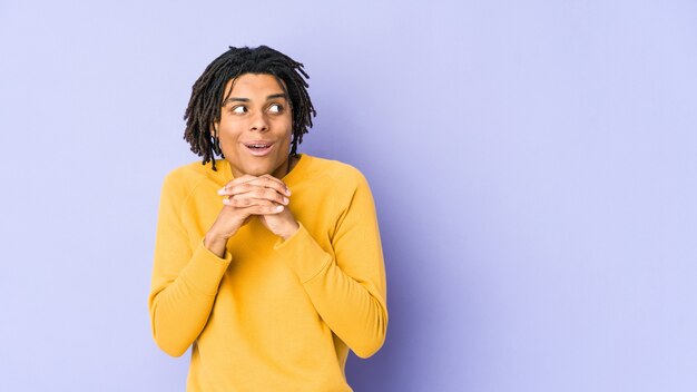 Jeune homme noir portant une coiffure rasta priant pour la chance, étonné et ouvrant la bouche à l'avant.