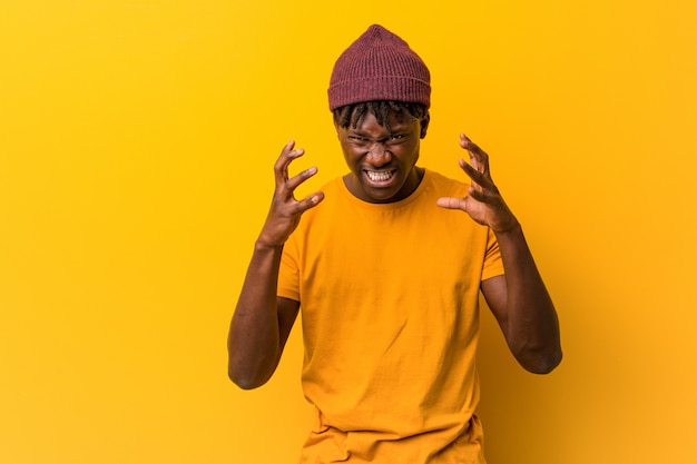 Jeune homme noir portant des rastas sur le mur jaune bouleversé crier avec des mains tendues.