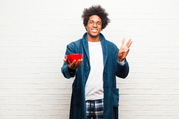 Jeune homme noir en pyjama avec un bol de petit déjeuner contre br