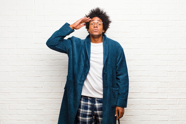 Jeune homme noir en pyjama avec une robe saluant la caméra avec un salut militaire en acte d'honneur et de patriotisme, montrant du respect