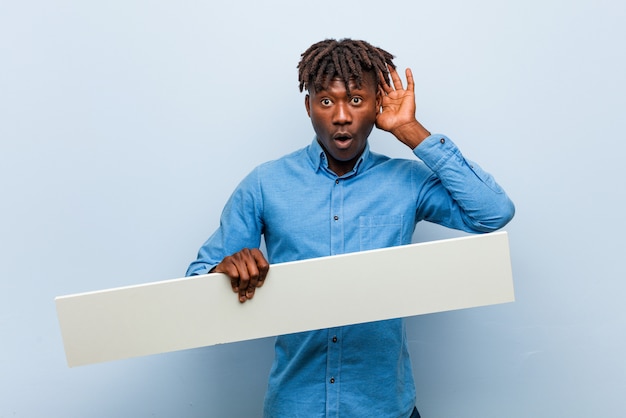 Jeune homme noir rasta tenant une pancarte essayant d'écouter un commérage.