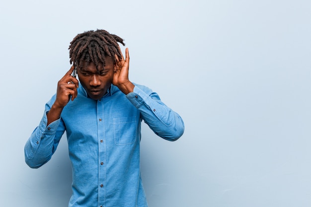 Jeune homme noir rasta tenant un téléphone essayant d'écouter un potin.