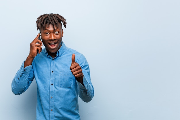 Jeune homme noir rasta tenant un téléphone souriant et levant le pouce vers le haut