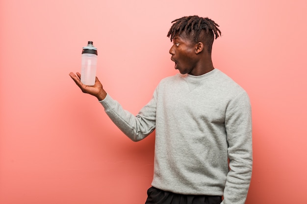 Jeune homme noir de remise en forme tenant une bouteille d'eau impressionné tenant l'espace copie sur la paume.