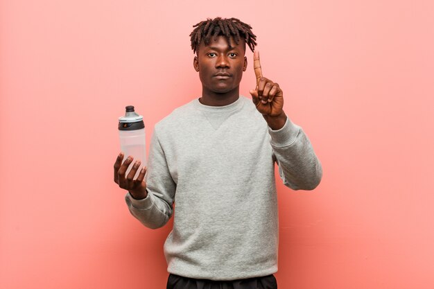 Jeune Homme Noir De Remise En Forme Tenant Une Bouteille D'eau Montrant Le Numéro Un Avec Le Doigt.