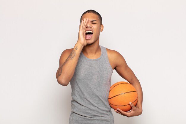 Jeune homme noir se sentant heureux, excité et positif, donnant un grand cri avec les mains à côté de la bouche, appelant