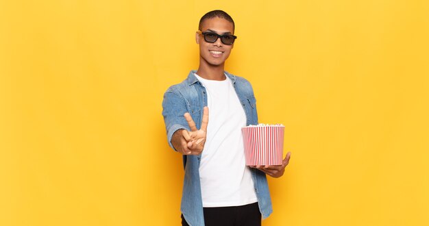 Jeune homme noir souriant et ayant l'air heureux, insouciant et positif, gesticulant la victoire ou la paix d'une main