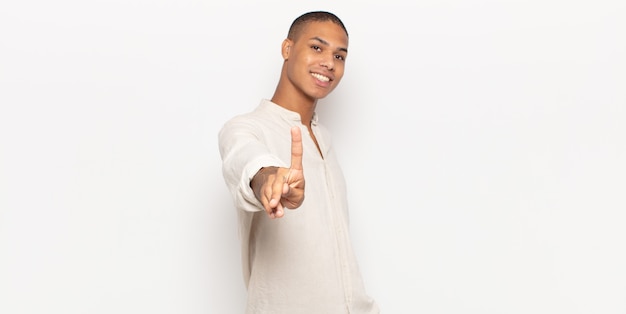 Jeune homme noir souriant fièrement et avec confiance en faisant le numéro un pose triomphalement, se sentant comme un leader