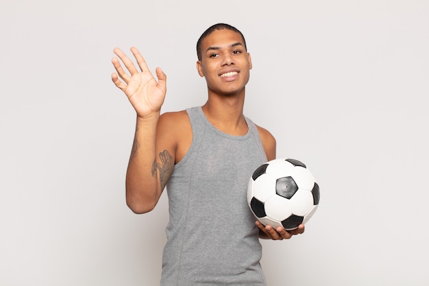 Jeune homme noir souriant joyeusement et gaiement, en agitant la main, en vous accueillant et en vous saluant, ou en vous disant au revoir