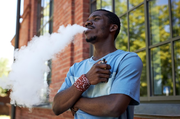 Jeune homme noir en t-shirt bleu clair fumant une cigarette électronique