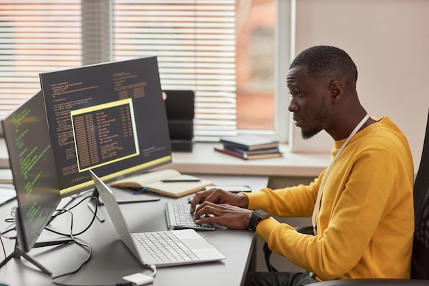 Photo jeune homme noir tapant au clavier et écrivant du code dans une société de développement informatique