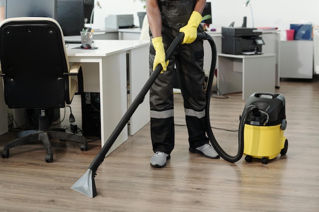 Jeune homme noir en uniforme et gants jaunes à l'aide d'un aspirateur