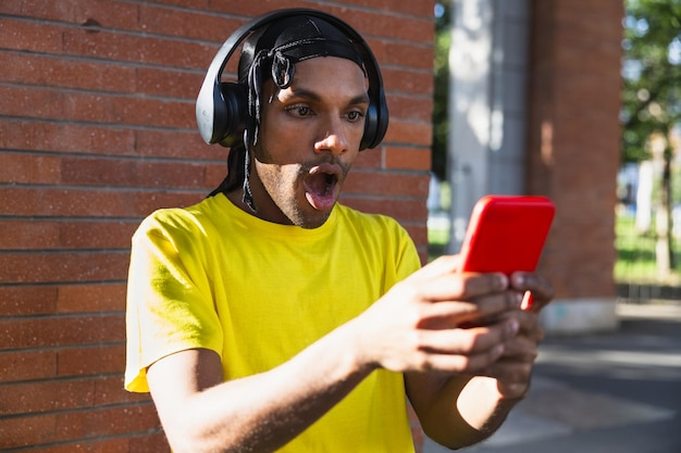 Jeune homme noir urbain avec un durag qui semble très surpris par ce qu'il voit sur son téléphone