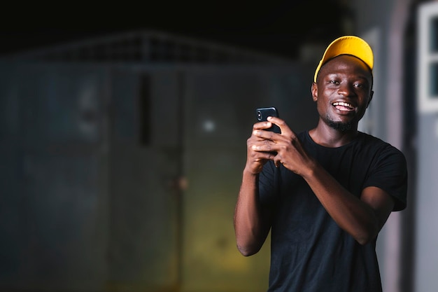 Jeune homme noir utilisant un appareil mobile tout en souriant à la caméra