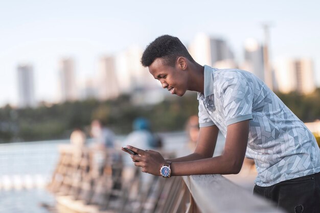 Jeune homme noir en vêtements décontractés tapant un sms avec son espace de copie de téléphone portable comprend