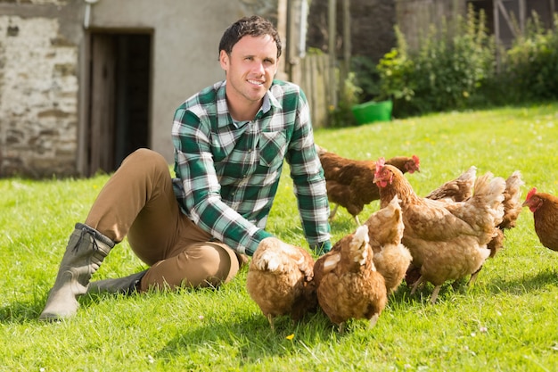 Jeune homme nourrir ses poules souriant à la caméra