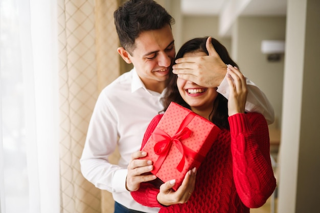 Un jeune homme offre un cadeau à sa bien-aimée et ferme les yeux d'une main