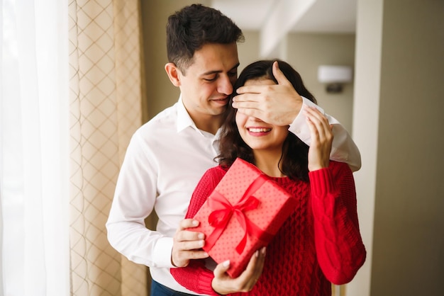 Un jeune homme offre un cadeau à sa bien-aimée et ferme les yeux d'une main