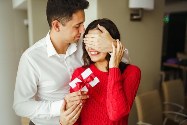 Un jeune homme offre un cadeau à sa bien-aimée et ferme les yeux d'une main