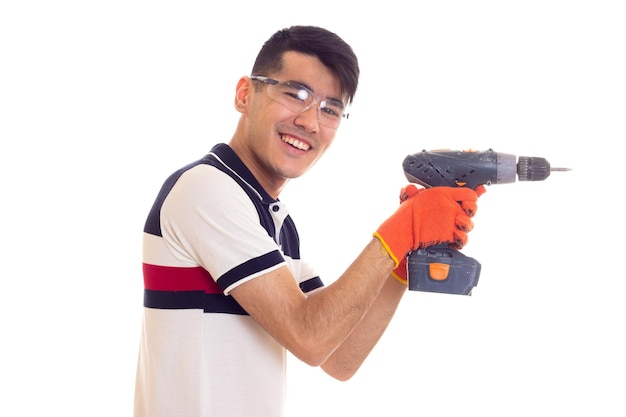 Jeune homme optimiste avec des gants orange et des lunettes de protection tenant un tournevis électrique gris