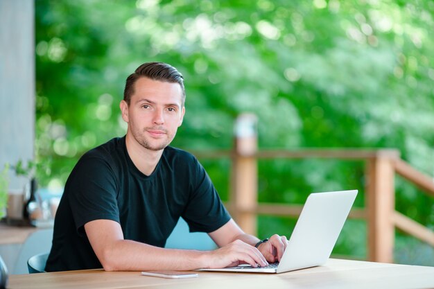 Jeune homme avec ordinateur portable au café en plein air, boire du café. Homme utilisant un smartphone mobile.