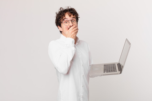 Jeune homme avec un ordinateur portable couvrant la bouche avec les mains avec un choc