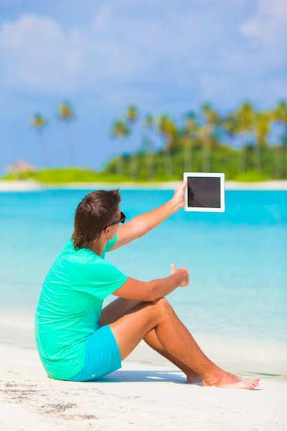 Jeune homme avec un ordinateur portable sur une plage tropicale