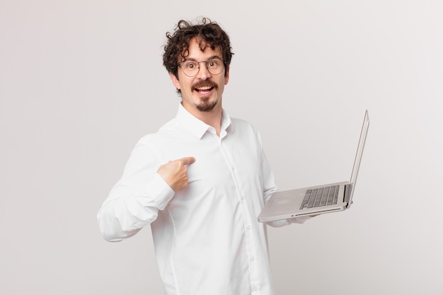 Jeune homme avec un ordinateur portable se sentant heureux et pointant vers lui-même avec un excité