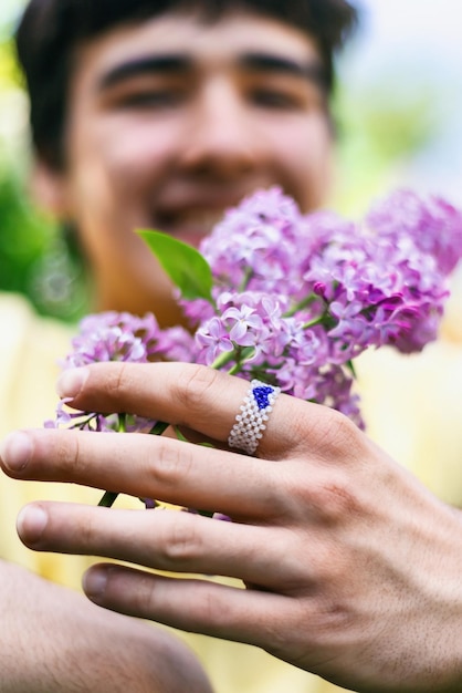 Un jeune homme d'orientation sexuelle non traditionnelle tient une fleur de lilas dans ses mains