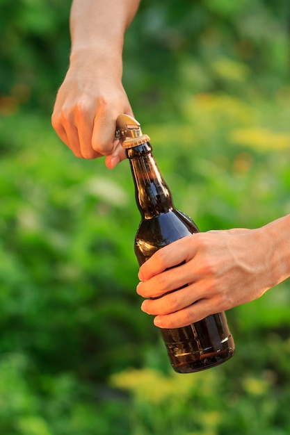 Le jeune homme ouvre la bouteille de bière avec le vieil ouvreur sur le fond brouillé naturel