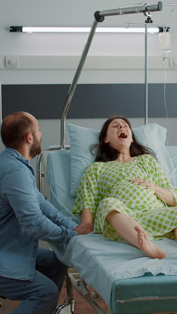 Jeune homme paniqué alors que sa femme enceinte a des contractions en salle d'hôpital. Un mari caucasien reçoit de l'aide médicale pour une femme qui crie de douleur. L'agonie et la douleur de l'accouchement