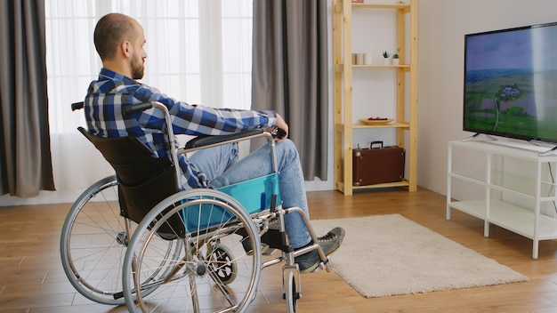 Jeune homme paralysé et déprimé en fauteuil roulant devant la télévision.