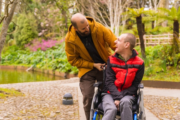 Jeune homme paralysé en fauteuil roulant poussé par un ami dans un parc public de la ville s'amusant au printemps