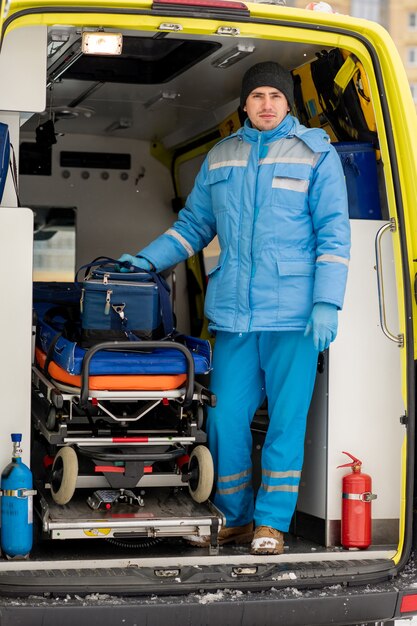 Jeune homme paramédical avec trousse de premiers soins debout par civière à l'intérieur de la voiture d'ambulance