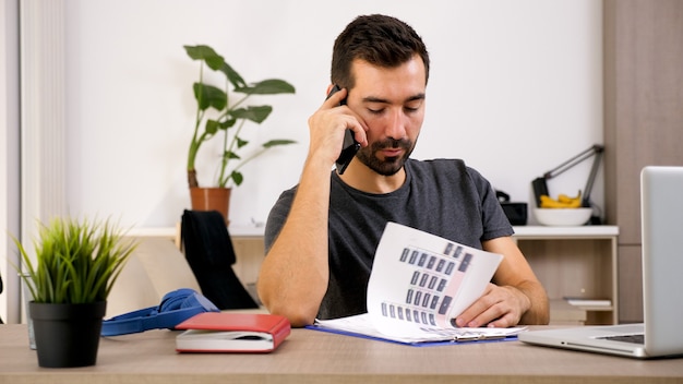 Jeune homme parlant au téléphone alors qu'il est au bureau. Homme intelligent prenant soin des affaires.