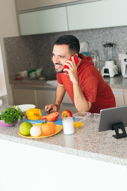 Jeune homme parlant au téléphone portable tout en préparant le petit déjeuner à la maison